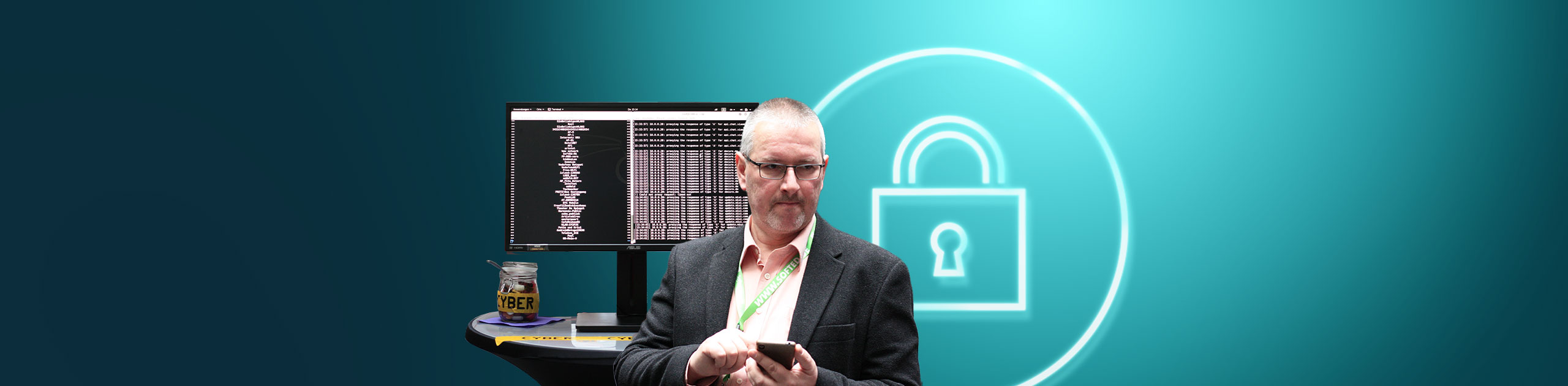 Ulf Riechen mit Smartphone vor einem Monitor mit Programmiercode, daneben ein Tisch mit einem Glas mit „CYBER“-Beschriftung; im Hintergrund ein stilisiertes Schloss-Symbol auf türkisfarbenem Verlauf.